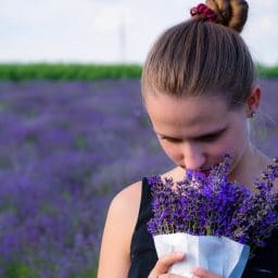 a woman smelling a bunch of lavender next to a field of lavender