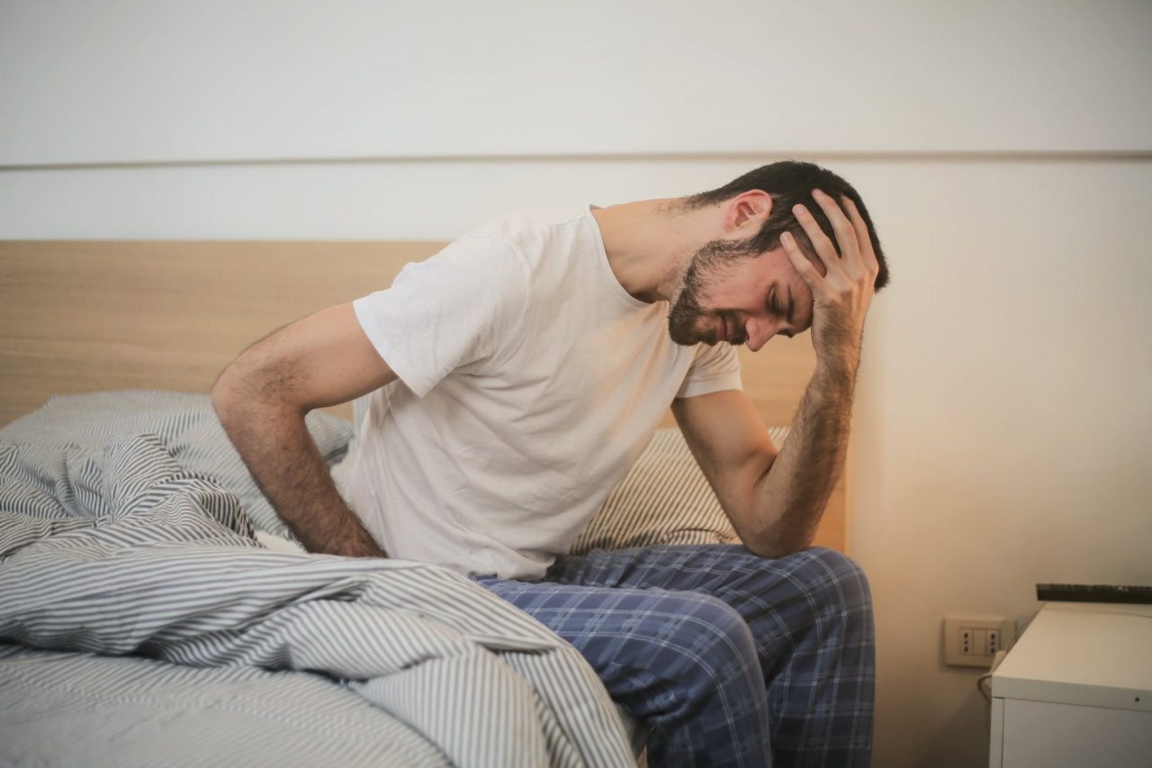Man with a headache sits on the edge of his bed.
