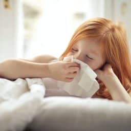 Little girl blowing her nose while in bed.