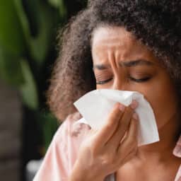 Woman with allergies sneezing into a tissue.