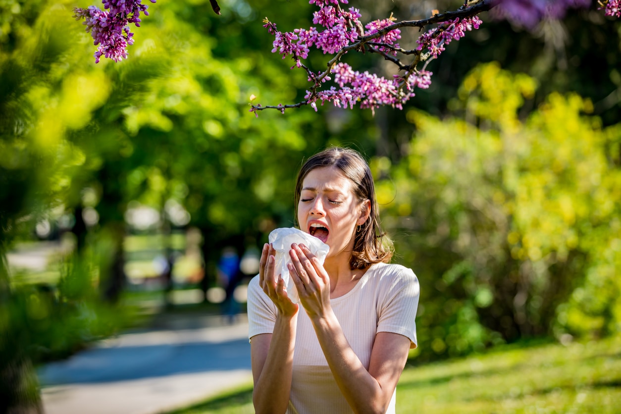 Young woman sneezing outdoors.