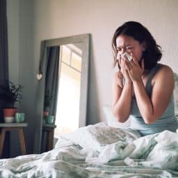 Woman with allergies blowing her nose in bed.