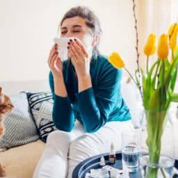 Woman sitting next to her cat, sneezing into a tissue