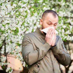 Man blowing his nose around floral trees in the park
