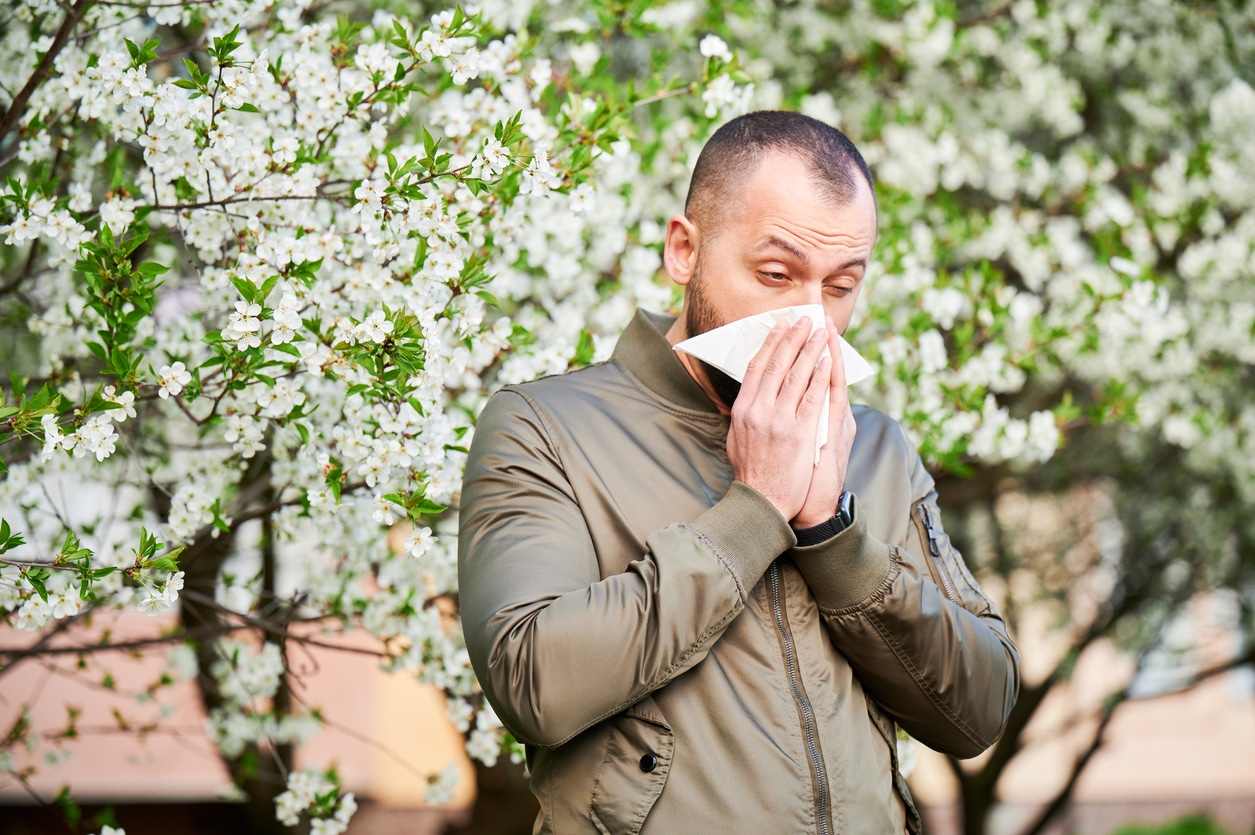 Man blowing his nose around floral trees in the park.