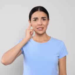 Woman pointing to her ear looking concerned