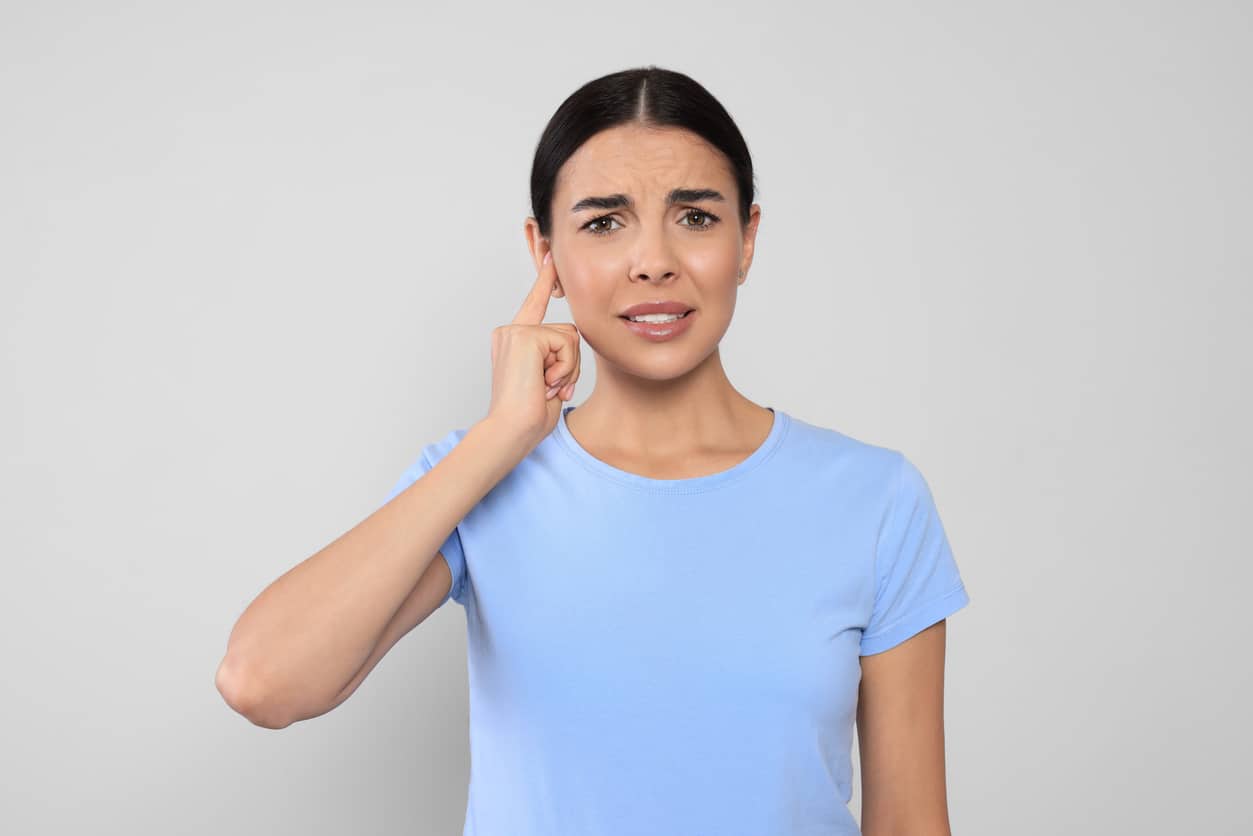Woman pointing to her ear looking concerned.