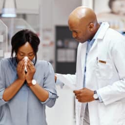 Allergy specialist talking to a patient who's blowing her nose.